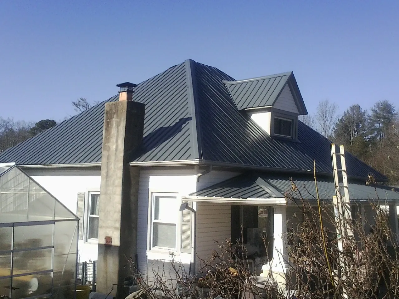Dark blue standing seam metal roof on a white farmhouse with dormer — Slate & Tile Roof Repair by Roofing Brothers in Grasonville