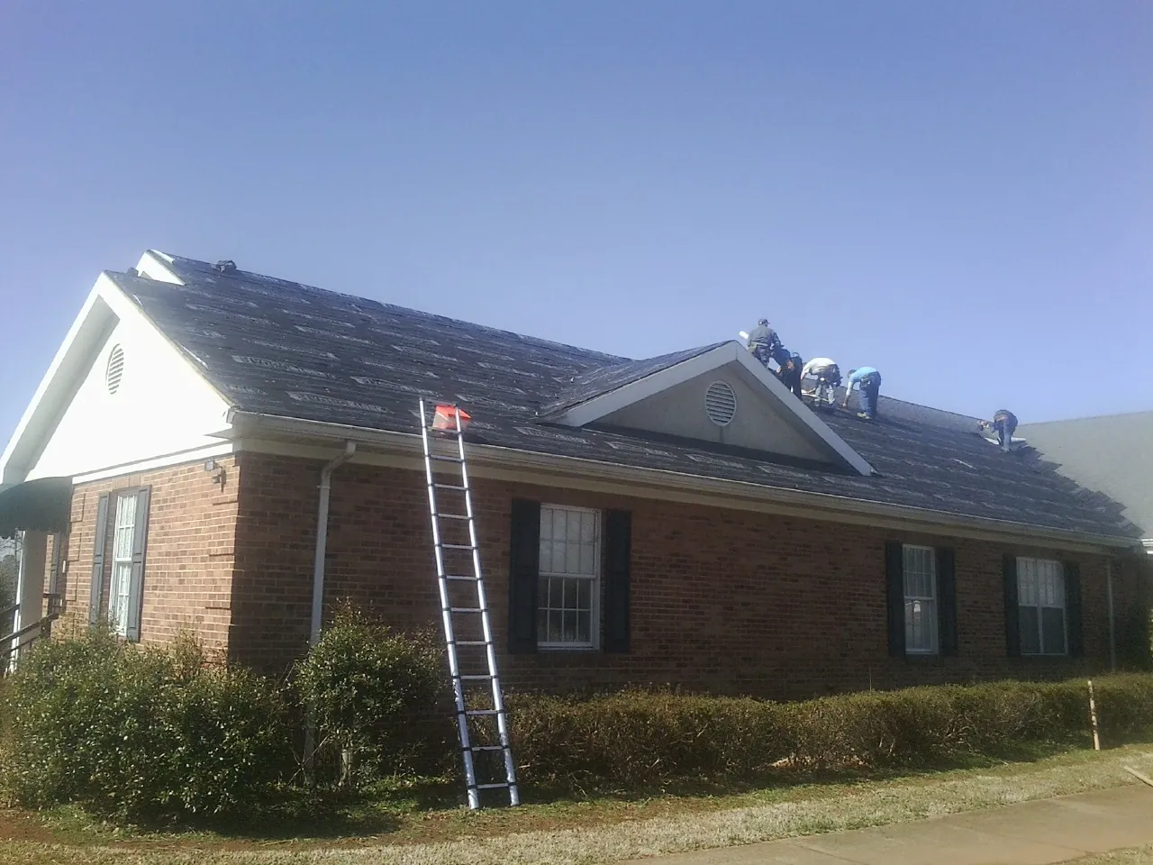 Crew tearing shingles off a brick ranch roof with a ladder set — Emergency Roof Repair work by our crew in Grasonville