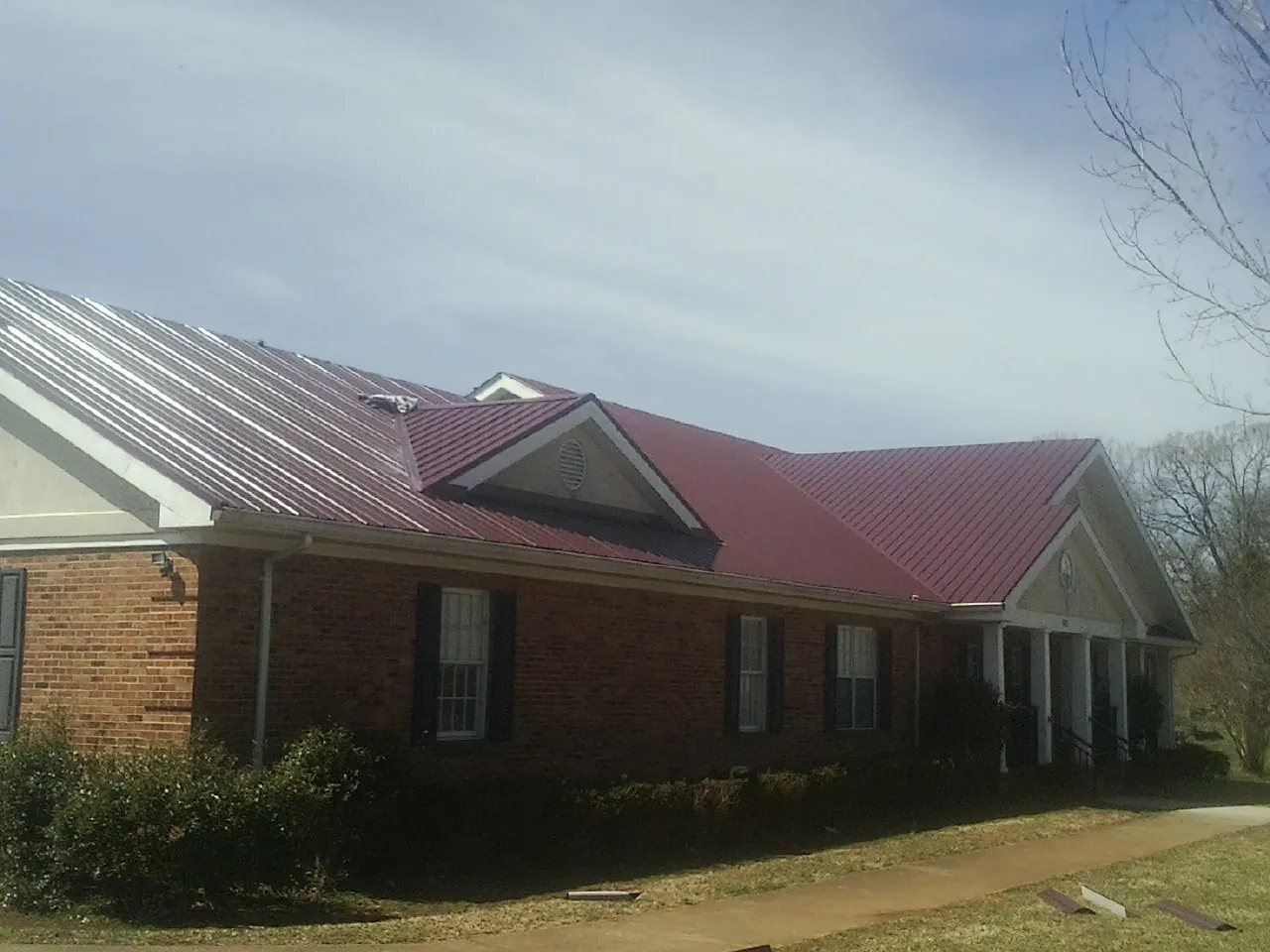 Red metal roof with gabled entries on a long brick building, from a Hail Damage Roof Repair job in Grasonville