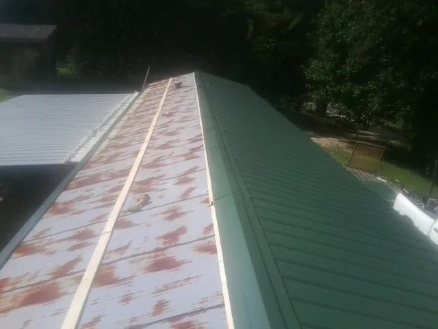 Old rusted panels beside newly installed green metal roofing — Wind Damage Roof Repair by Roofing Brothers in Grasonville