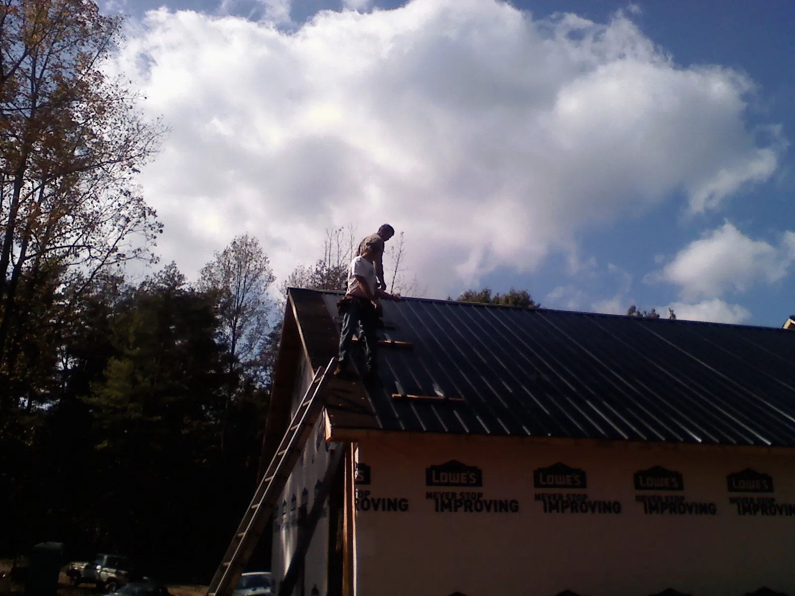 Roofer fastening dark metal panels high against a cloudy sky in Grasonville