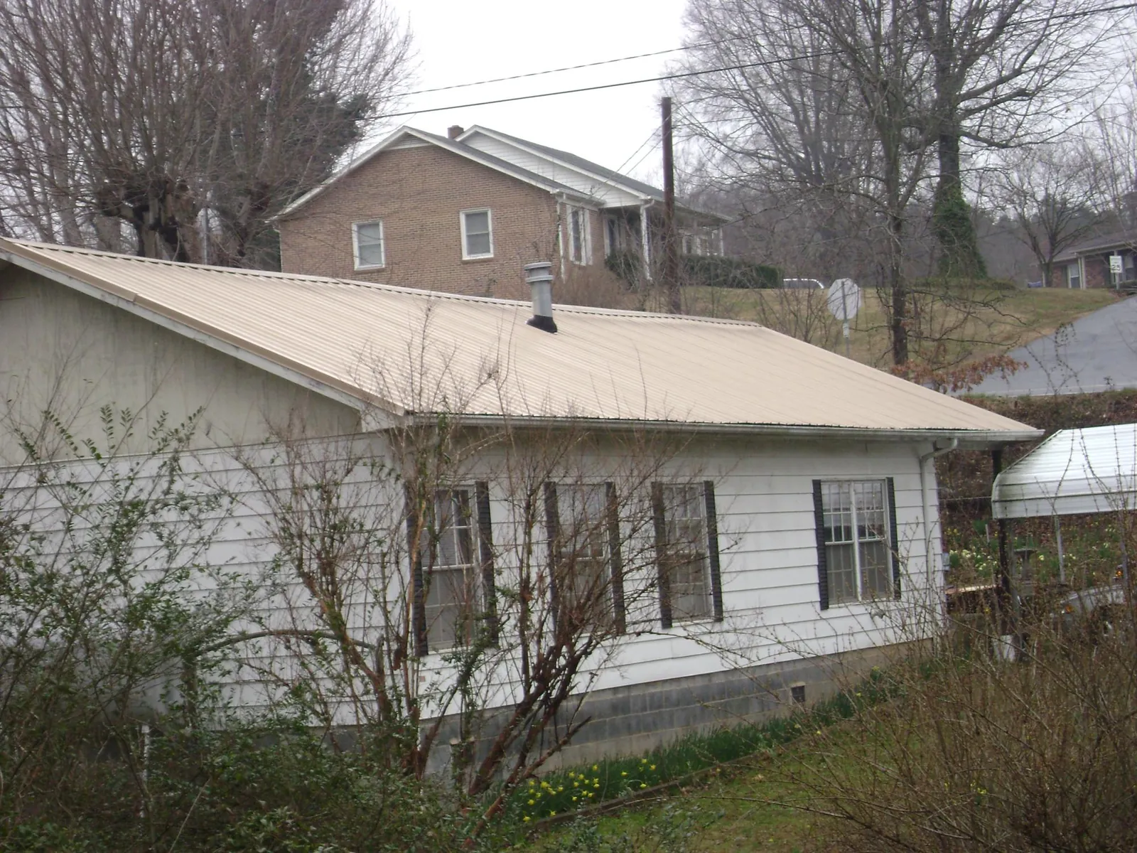 Tan metal roof on a white sided house set into a hillside — Commercial Roofing by Roofing Brothers in Grasonville